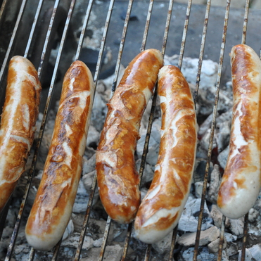 Fünf gegrillte Würste auf einem Grillrost über glühender Kohle.