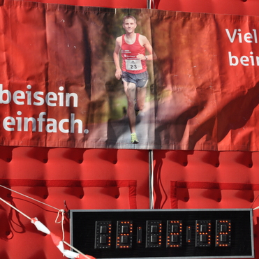 Banner mit motivierendem Spruch zum Laufen und einem Läufer, darunter ein Zeitmessgerät auf rotem Hintergrund.