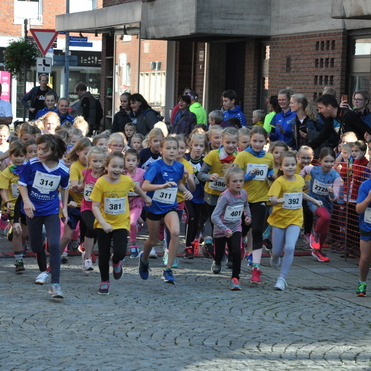 Zusammenlauf junger Mädchen in Wettkampfkleidung beim Start eines Laufes auf einer gepflasterten Straße.
