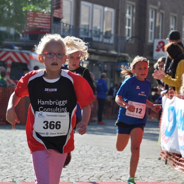 M&auml;dchen im roten Trikot l&auml;uft beim Citylauf, w&auml;hrend ein weiteres M&auml;dchen im blauen Shirt im Hintergrund mitl&auml;uft.