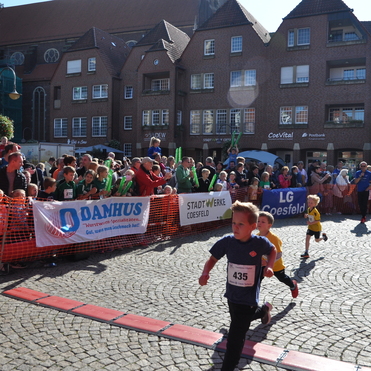 Zwei Kinder laufen w&auml;hrend eines Wettlaufs unter einem roten Zielbogen, Zuschauer feuern sie an.