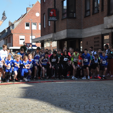 Startsignal f&uuml;r einen Laufwettbewerb mit vielen Athleten in blauen und schwarzen Trikots auf einer Stra&szlig;e.