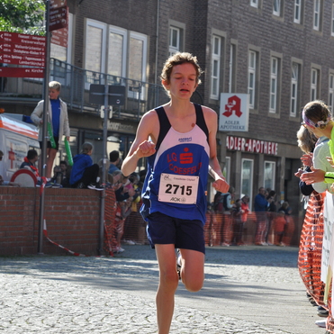 Ein Jugendlicher l&auml;uft mit einer Startnummer auf einem Wettkampfkurs in einer st&auml;dtischen Umgebung.