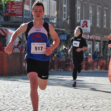 Junger L&auml;ufer mit der Startnummer 517 sprintet auf einer Laufstrecke, w&auml;hrend ein weiterer Athlet im Hintergrund folgt.