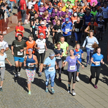 Gruppenszene eines Laufes mit vielen Teilnehmenden in bunten Shirts, umgeben von jubelnden Zuschauern.