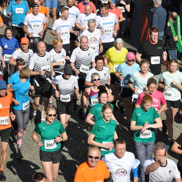 Eine gro&szlig;e Gruppe von Teilnehmern l&auml;uft bei einem Stra&szlig;enlauf, alle in verschiedenen Sportoutfits und Startnummern.