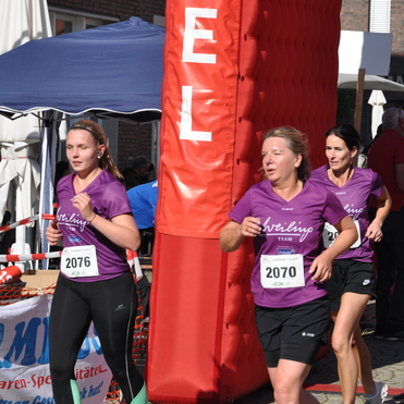Drei Frauen in lila T-Shirts und ein Junge in einem blauen Trikot laufen bei einem Wettkampf durch das Zieltor.