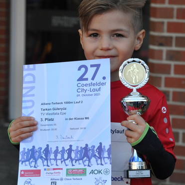 Junge mit kurzem Haar h&auml;lt Pokal und Urkunde f&uuml;r den 3. Platz beim 27. Coesfelder City-Lauf.