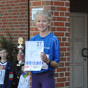 M&auml;dchen mit Pokal und Urkunde, l&auml;chelnd vor Ziegelwand, nach dem 27. Coesfelder City-Lauf.