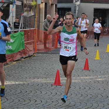 L&auml;ufer mit der Nummer 3671 zeigt das Peace-Zeichen w&auml;hrend eines Wettkampfs auf einer gepflasterten Stra&szlig;e.