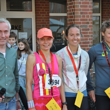 Vier Personen stehen l&auml;chelnd vor einer Backsteinwand, nach einem Laufwettbewerb, Medaillen um den Hals.