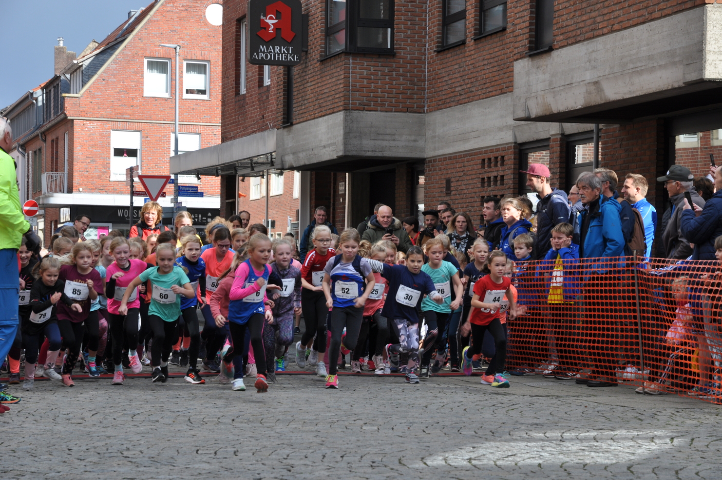 Gruppe von Kindern in Sportkleidung startet beim Laufevent in einer Innenstadt, umgeben von Zuschauern.