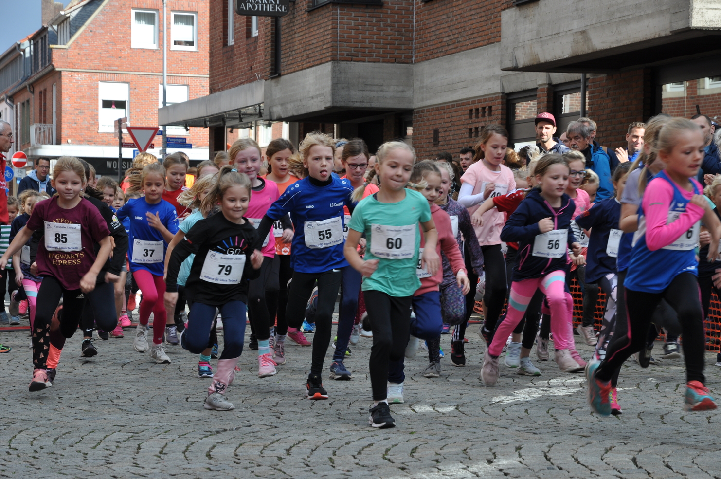 Mädchenlauf mit zahlreiche Teilnehmerinnen in Sportbekleidung, die auf einer Stadtstraße in Richtung Kamera rennen.