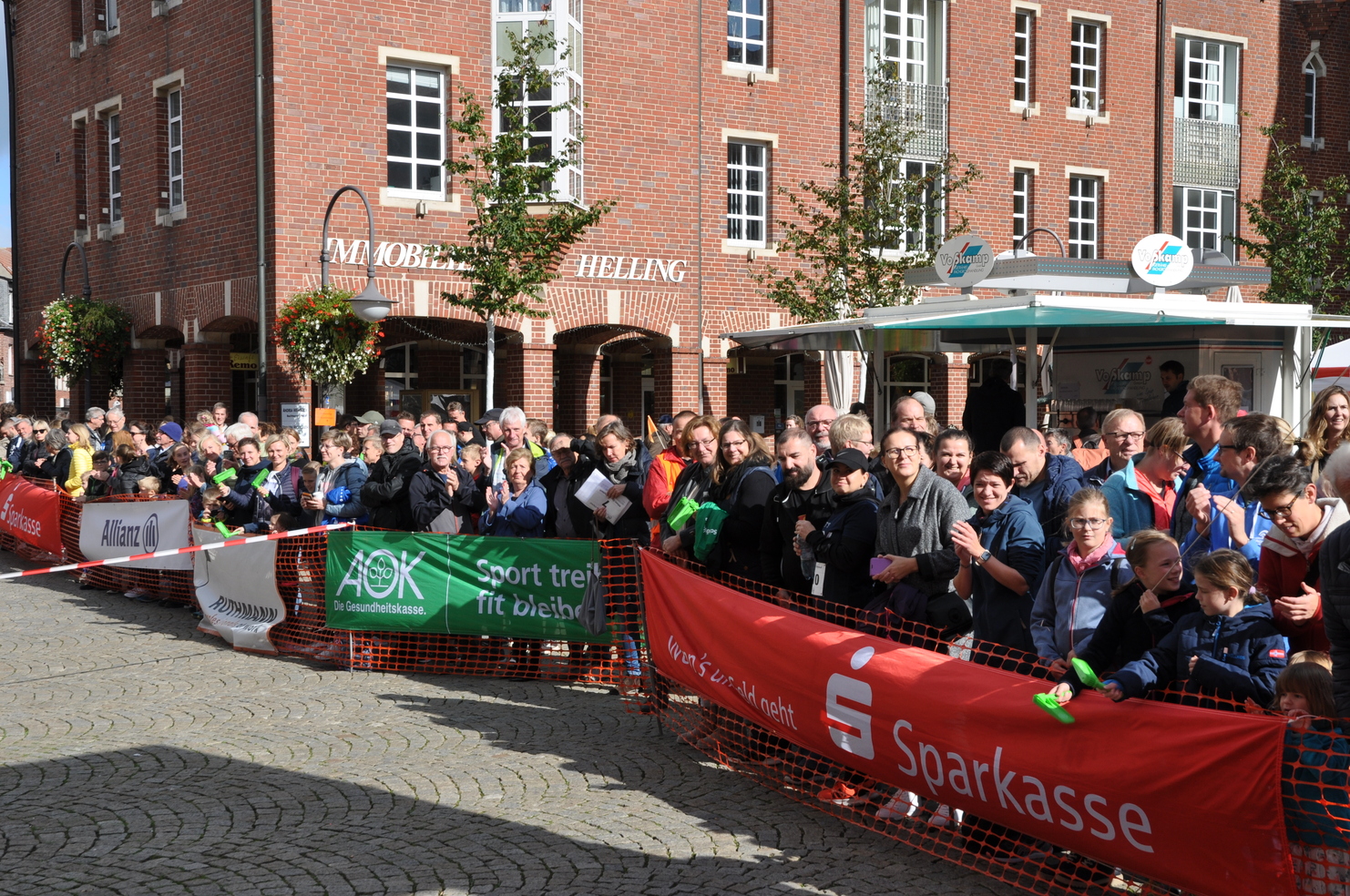 Große Menschenmenge beim Event, umgeben von Werbebannern und Backsteingebäuden, auf einem gepflasterten Platz.