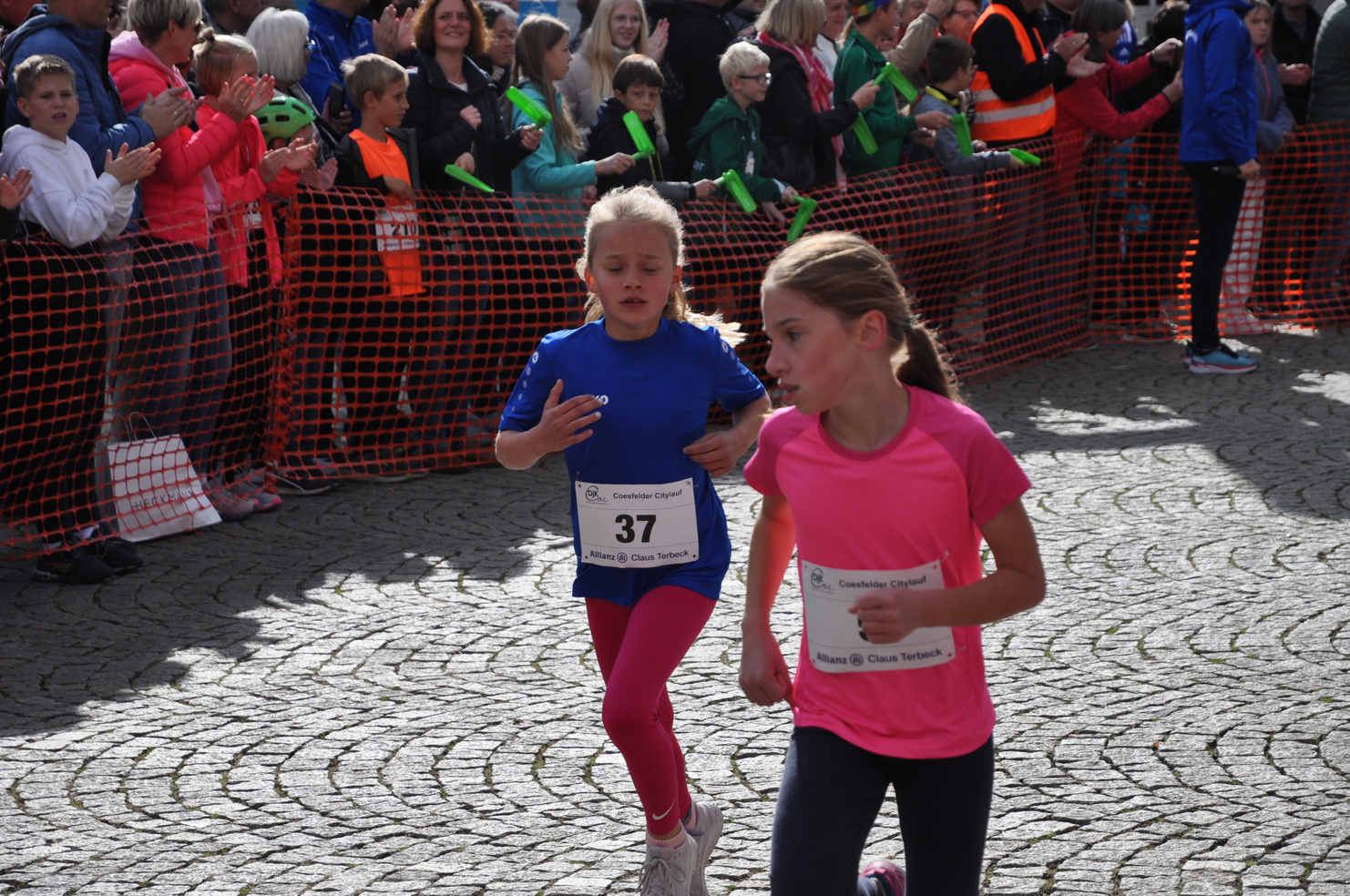 Zwei Mädchen in Sportkleidung laufen beim Coesfelder Citylauf, umgeben von applaudierenden Zuschauern.
