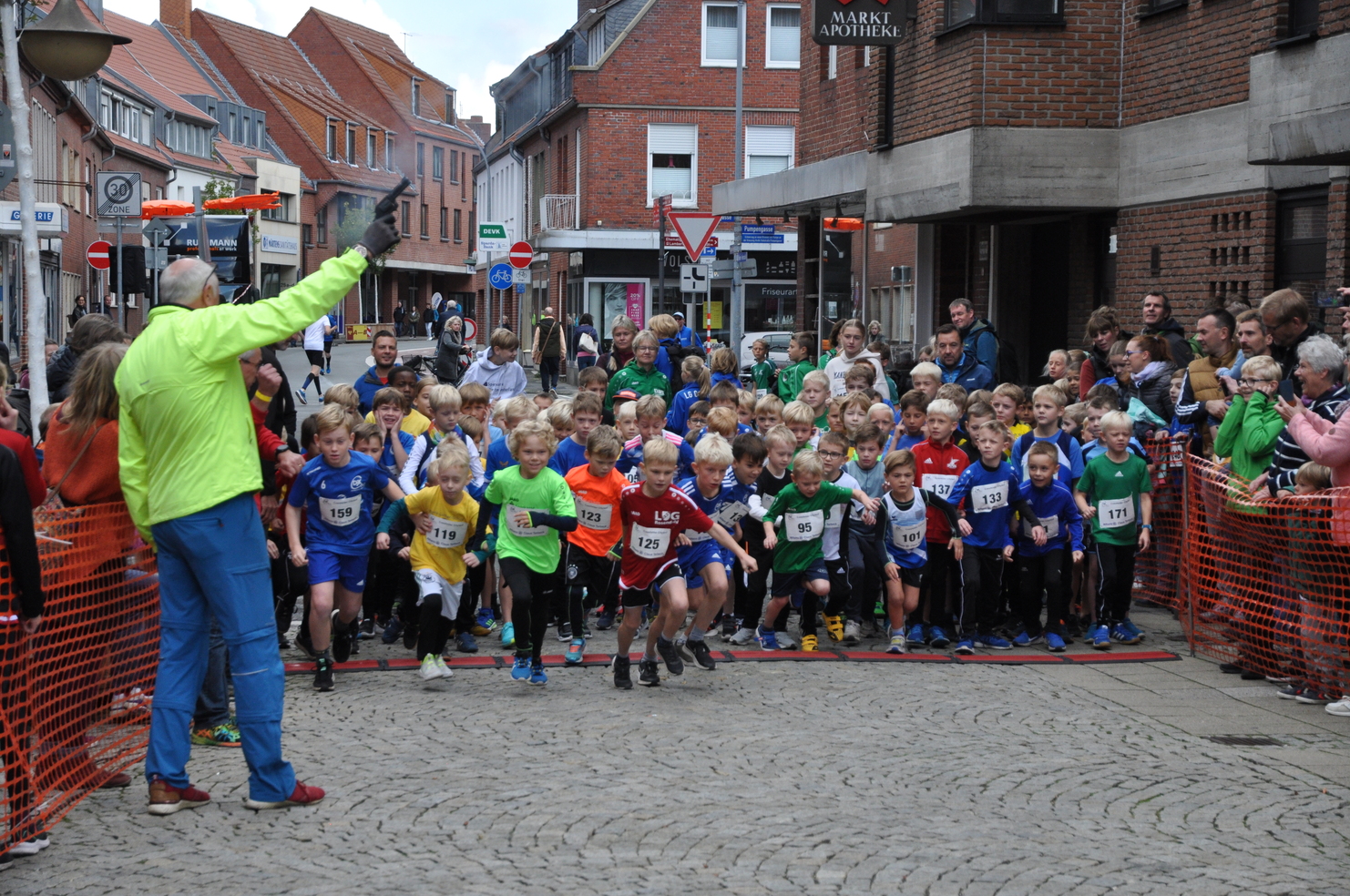 Startschuss für ein Kinderlauf-Event, zahlreiche Teilnehmer in bunten Trikots und aufgeregte Zuschauer am Straßenrand.