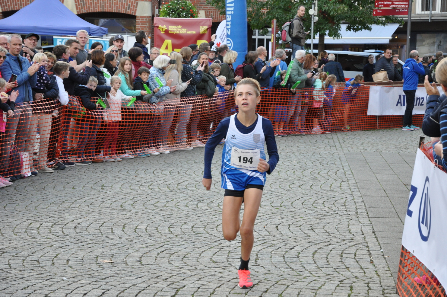Ein junger Läufer mit Startnummer 194 läuft auf einem Wettkampf, während Zuschauer hinter einer Absperrung anfeuern.