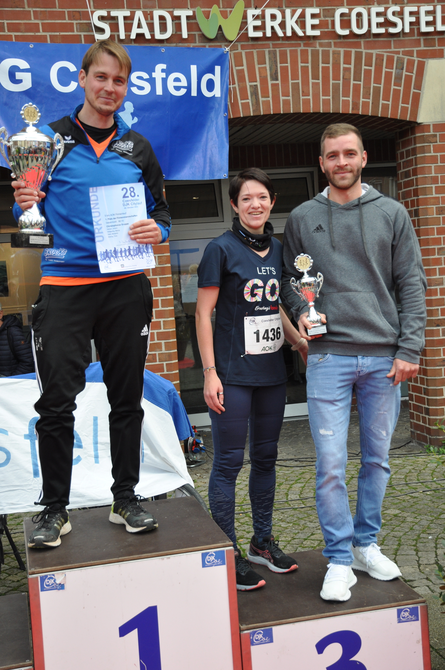 Drei Läufer auf dem Siegertreppchen halten Pokale und Urkunden nach einem Wettkampf in Coesfeld.