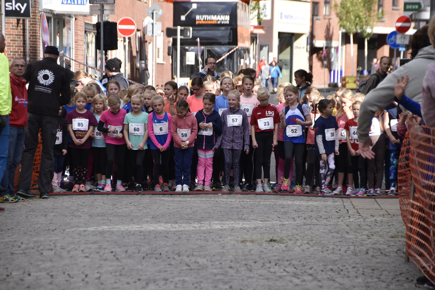 Gruppe von Mädchen in Sportkleidung steht an einer Startlinie für ein Rennen in einer Stadtstraße.