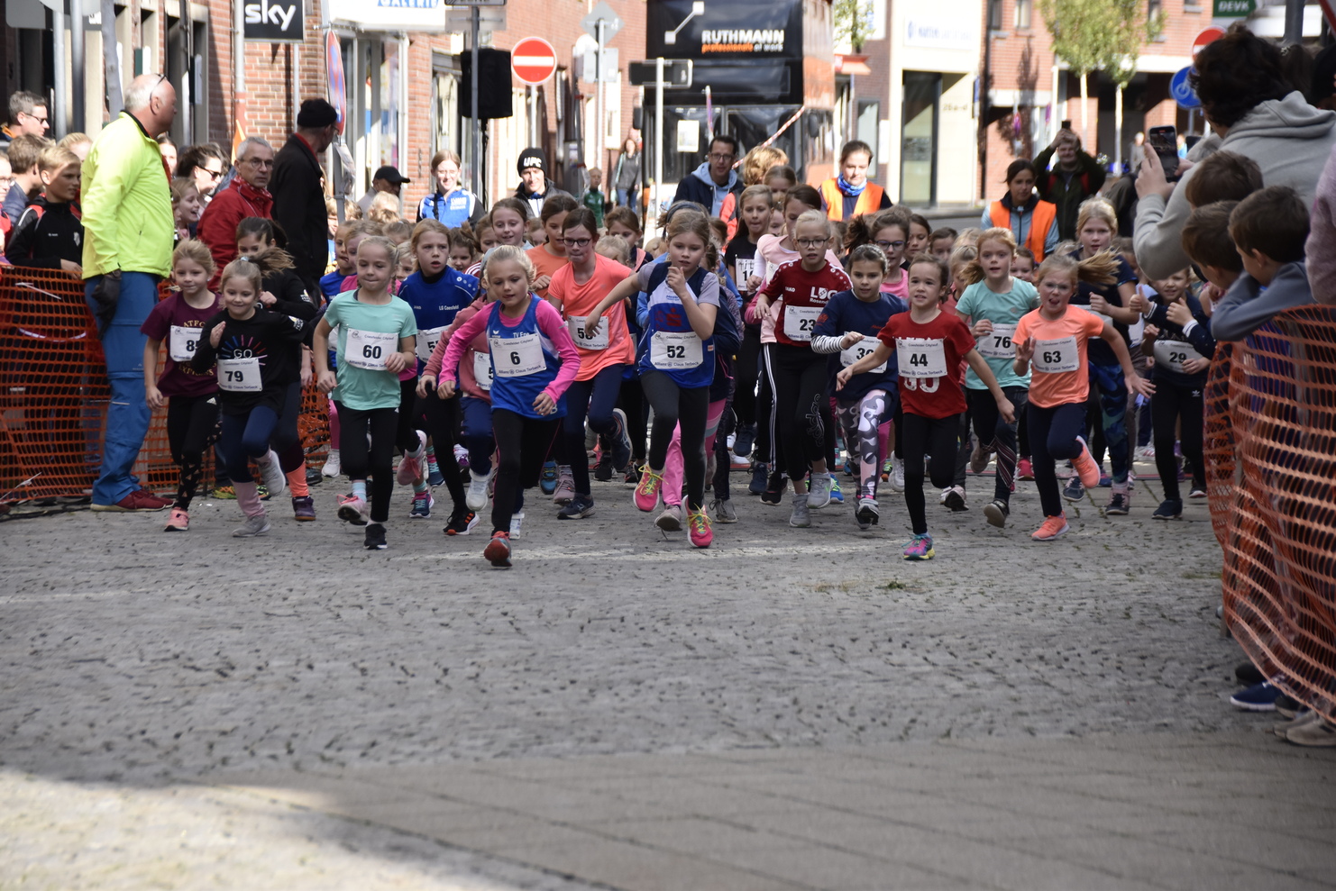 Start einer Kinderlaufveranstaltung mit zahlreichen Mädchen in Sportkleidung, die auf einer gepflasterten Straße laufen.