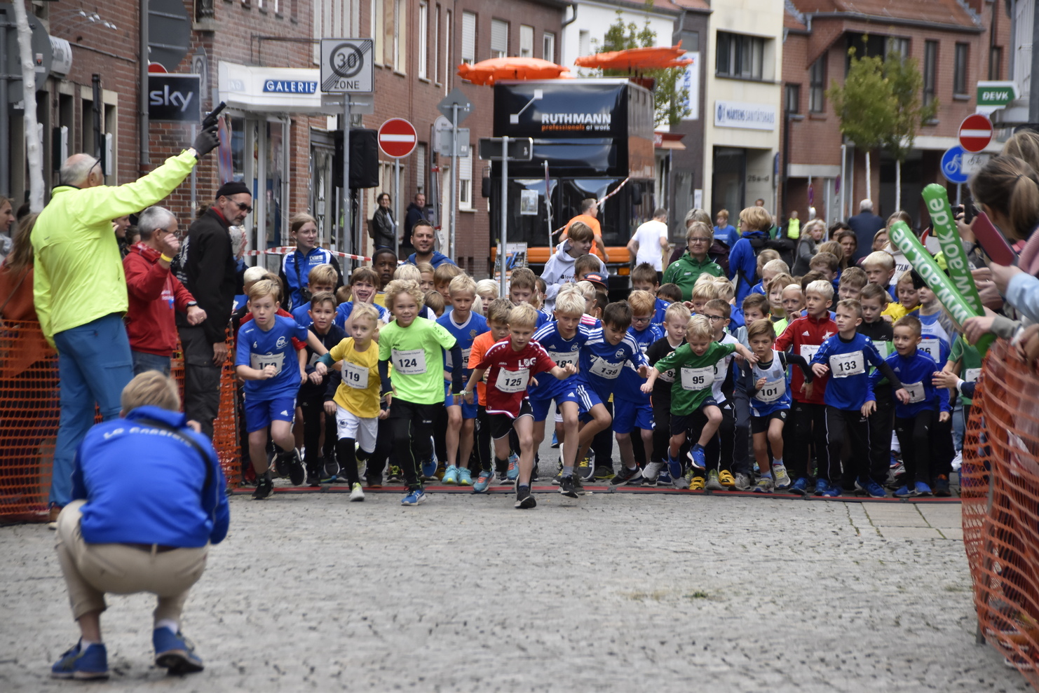 Startschuss für einen Kinderlauf mit vielen jungen Teilnehmern in bunten Trikots auf einer Straßensportveranstaltung.