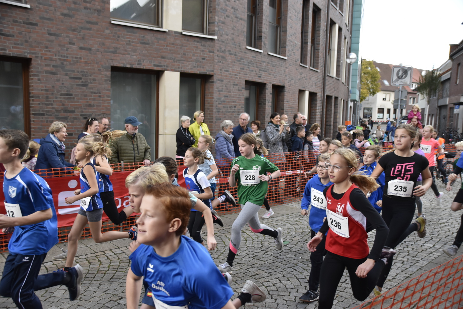 Kinderlauf mit jungen Teilnehmern in Sportbekleidung, umgeben von Zuschauern in einer städtischen Umgebung.