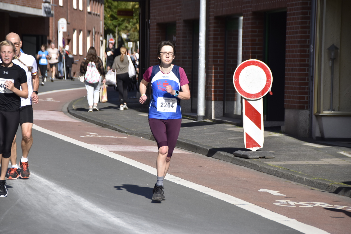 Läuferin mit Startnummer 2204 joggt auf einer Straße, umgeben von Zuschauern und Verkehrszeichen.