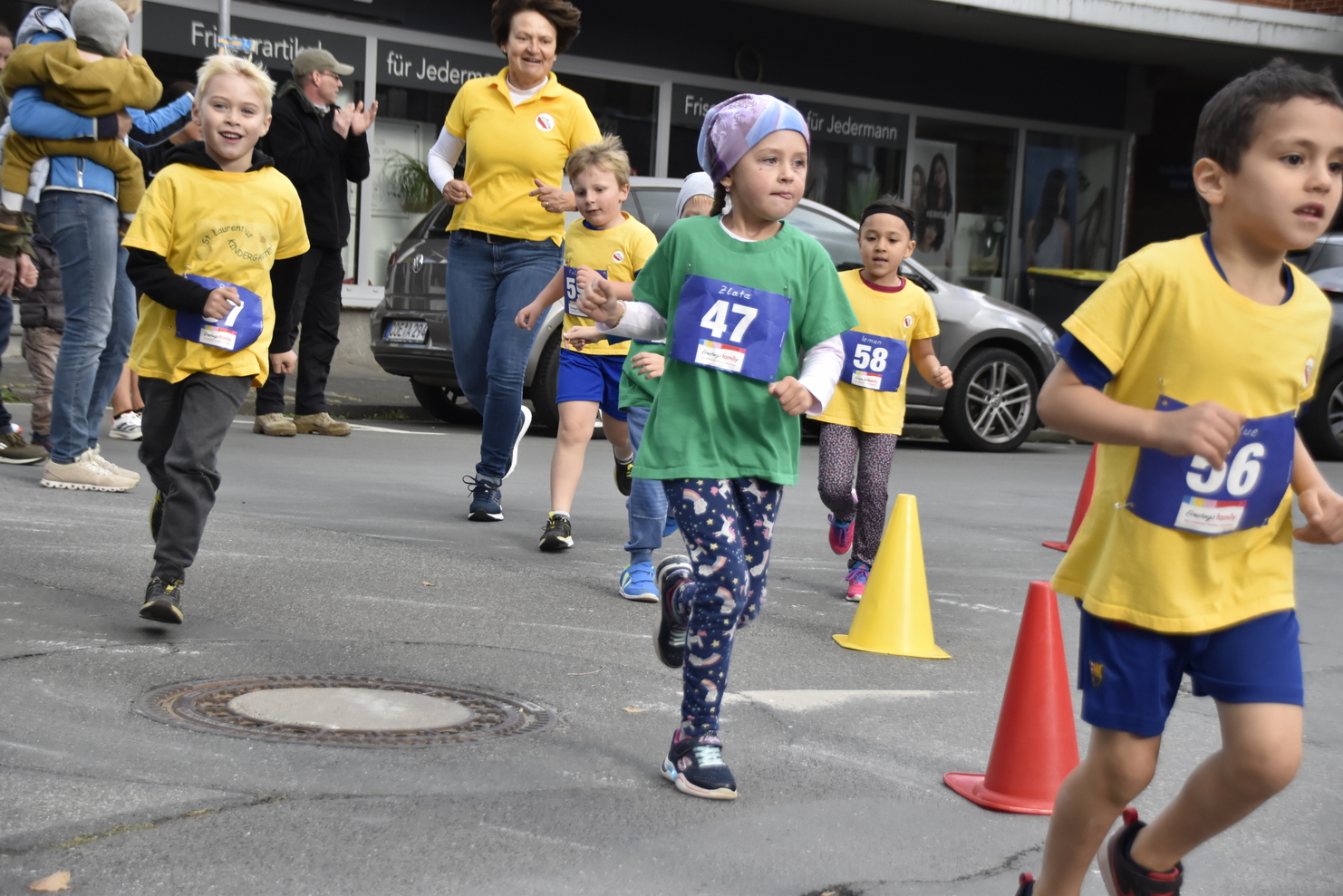 Kinder in gelben und grünen Shirts laufen beim Wettbewerb, umgeben von Zuschauern und gelben Absperrkegeln.