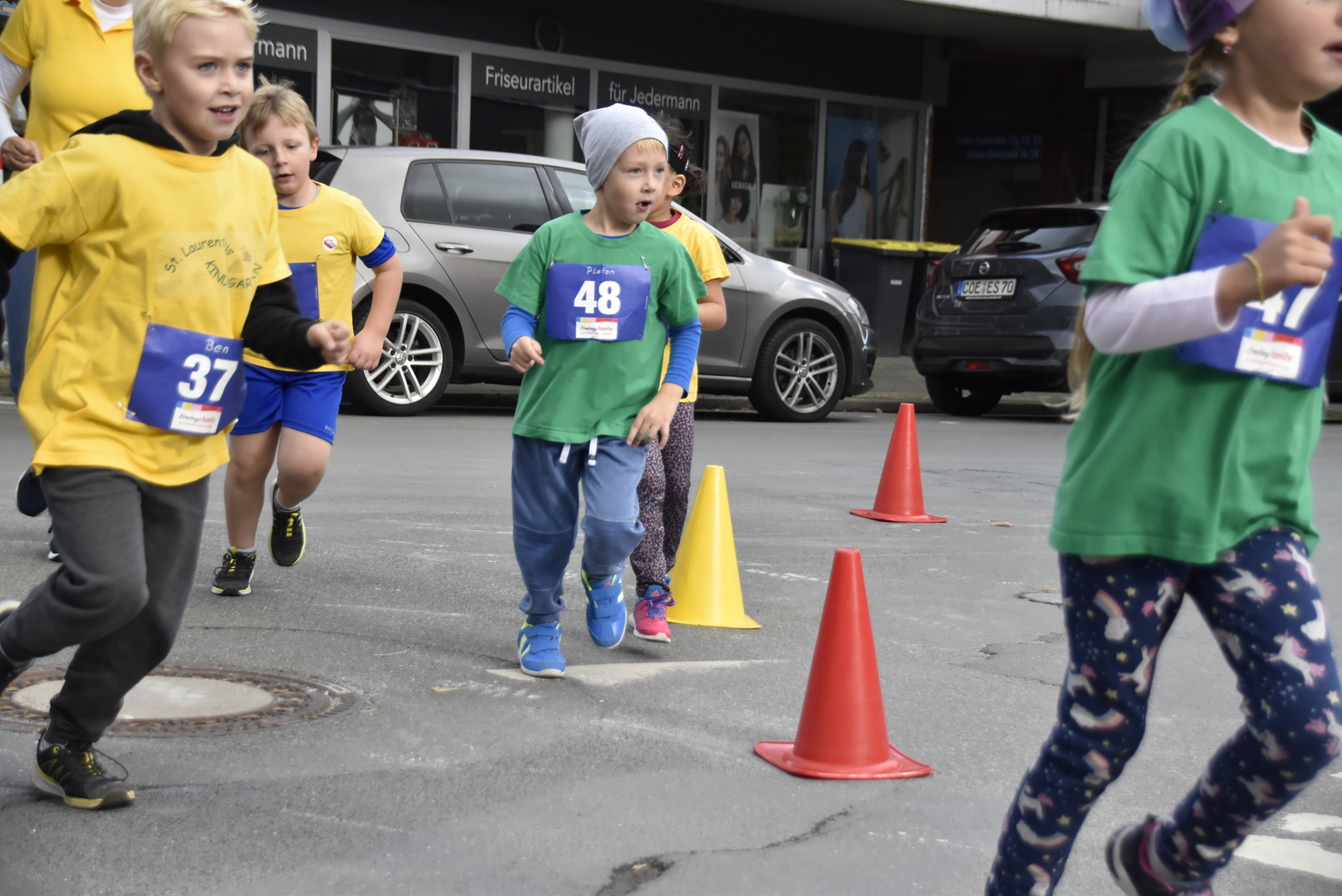 Kinder in Laufshirts nehmen an einem Wettlauf teil, während Verkehrshütchen auf dem Weg stehen.