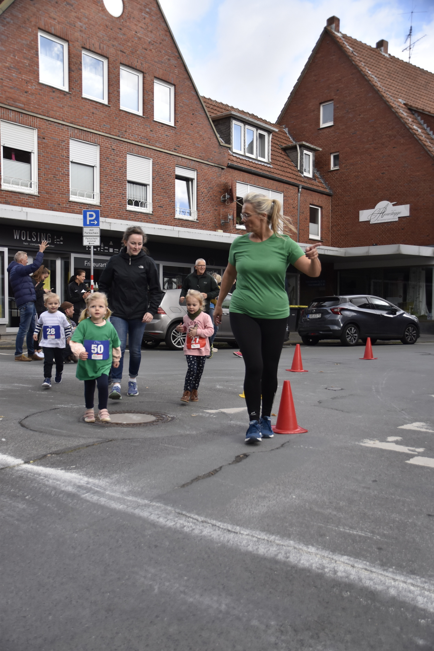 Kinder und Erwachsene laufen gemeinsam auf einer Straße, umgeben von orangefarbenen Pylonen und Zuschauern.