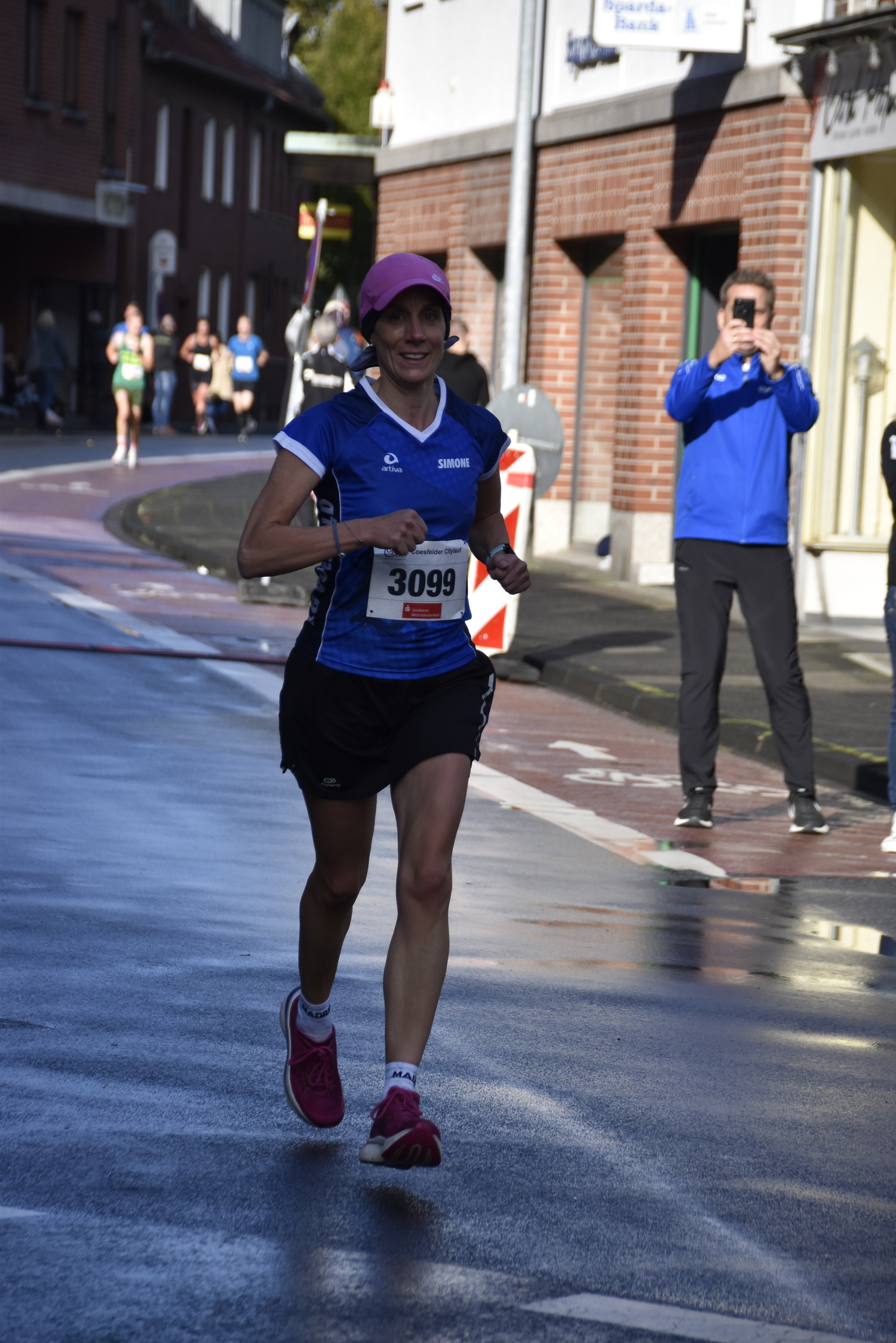 Läuferin mit Nummer 3099 in blauer Sportbekleidung joggt auf einer nassen Straße während eines Ereignisses.