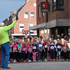 Gruppierung von Mädchen in Sportkleidung, die am Start eines Laufwettbewerbs an einer Straße warten.