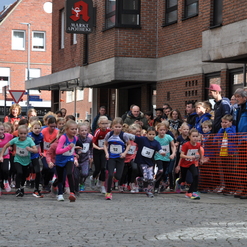 Gruppe von Kindern in Sportkleidung startet beim Laufevent in einer Innenstadt, umgeben von Zuschauern.