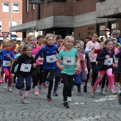 Mädchenlauf mit zahlreiche Teilnehmerinnen in Sportbekleidung, die auf einer Stadtstraße in Richtung Kamera rennen.