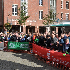 Große Menschenmenge beim Event, umgeben von Werbebannern und Backsteingebäuden, auf einem gepflasterten Platz.