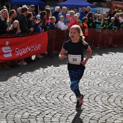 Mädchen mit Startnummer 31 läuft auf einem Wettkampf, umgeben von jubelnden Zuschauern und einer roten Werbebande.