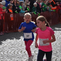 Zwei Mädchen in Sportkleidung laufen beim Coesfelder Citylauf, umgeben von applaudierenden Zuschauern.