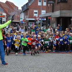 Startschuss für ein Kinderlauf-Event, zahlreiche Teilnehmer in bunten Trikots und aufgeregte Zuschauer am Straßenrand.