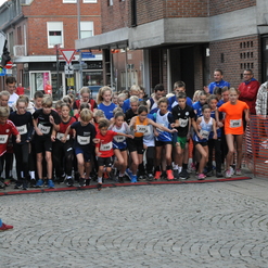 Start einer Kinder-Laufveranstaltung mit jungen Teilnehmern an einer gepflasterten Straße und Zuschauern im Hintergrund.