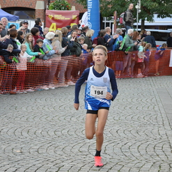 Ein junger Läufer mit Startnummer 194 läuft auf einem Wettkampf, während Zuschauer hinter einer Absperrung anfeuern.