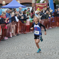 Junger Läufer in Sportbekleidung rennt auf einer gepflasterten Straße, Zuschauer feuern ihn an.