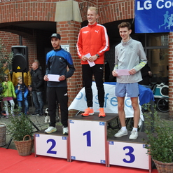 Drei Läufer stehen auf dem Siegertreppchen mit Platznummern, während Zuschauer im Hintergrund applaudieren.