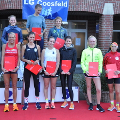 Gruppenfoto von Läuferinnen mit Urkunden bei der Siegerehrung vor einem Gebäude, roter Teppich und LG Coesfeld Banner im Hintergrund.