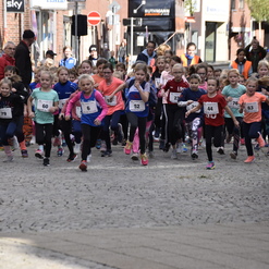 Start einer Kinderlaufveranstaltung mit zahlreichen Mädchen in Sportkleidung, die auf einer gepflasterten Straße laufen.