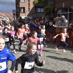 Eine Gruppe junger Läuferinnen startet beim Stadtlauf, umgeben von zuschauenden Menschen und einer festlichen Stimmung.