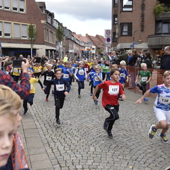 Kinder in Sportbekleidung laufen mit Freude eine Straße entlang, während Zuschauer entlang der Strecke stehen.