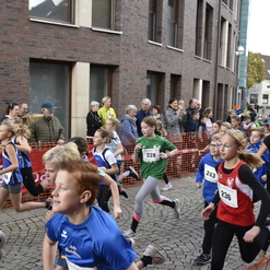 Kinderlauf mit jungen Teilnehmern in Sportbekleidung, umgeben von Zuschauern in einer städtischen Umgebung.