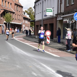 Läufer in Wettkampfkleidung beim Marathon auf einer Stadtstraße, umgeben von Zuschauern und Straßenverkehr.