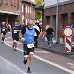 Läufer in sportlicher Kleidung winkt bei einem Wettbewerb auf einer städtischen Straße, umgeben von weiteren Teilnehmern.