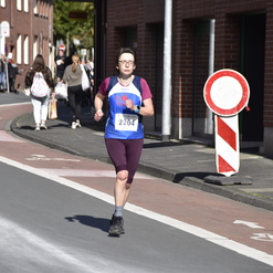 Läuferin mit Startnummer 2204 joggt auf einer Straße, umgeben von Zuschauern und Verkehrszeichen.